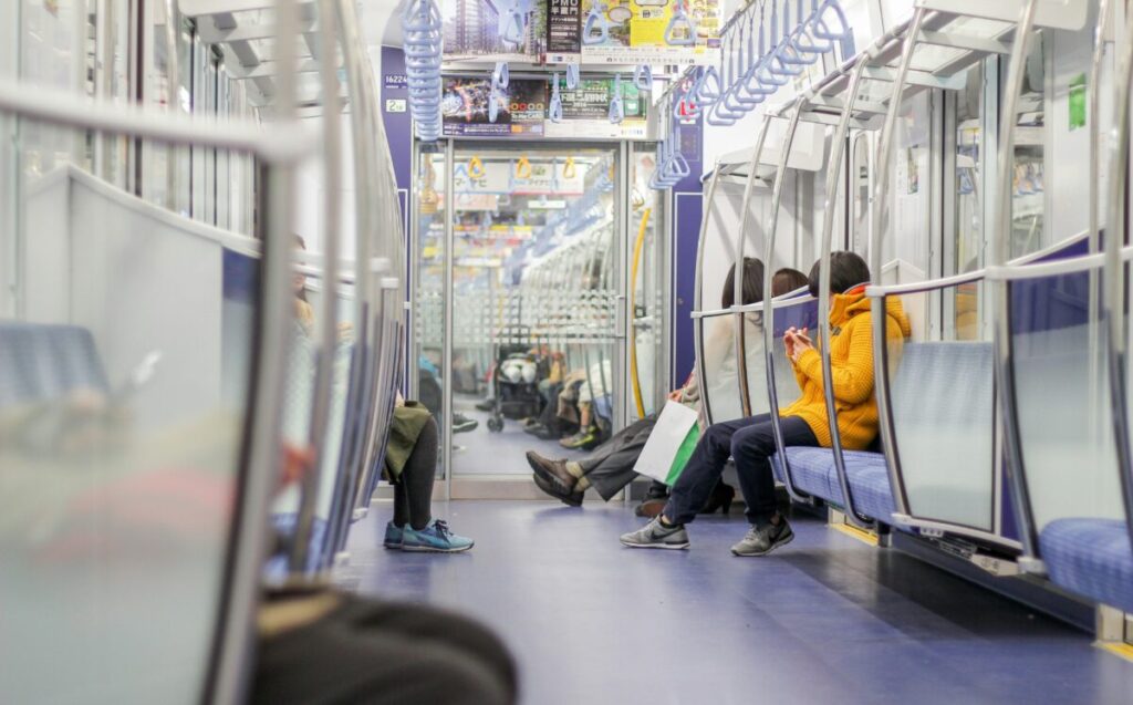It's a simple photograph showing people on their phones on a train in Japan. The image conveys the importance of needing a Japanese Phone Number when travelling around Japan.
