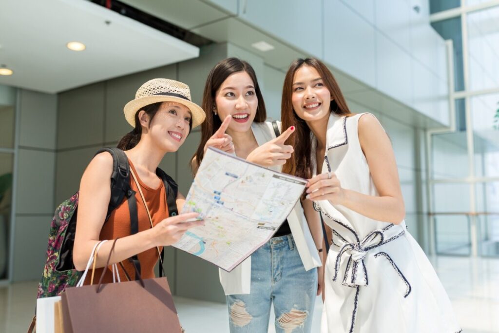 Three women on a trip in Japan looking at a map and pointing for directions in a modern indoor setting.