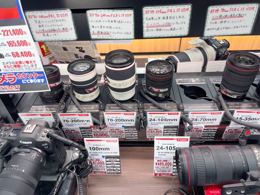 Canon RF camera lenses and a Canon EOS R3 displayed on a counter in a Japanese electronics shop.