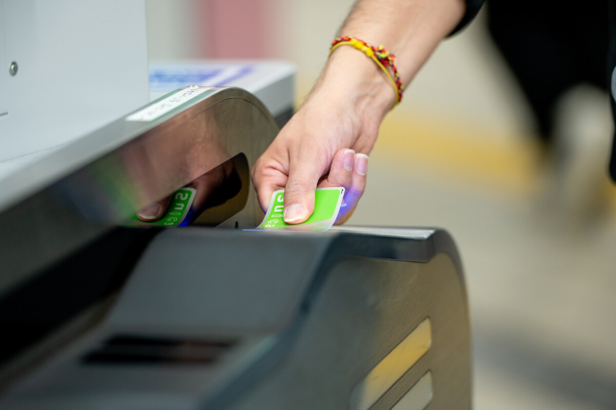 Traveller tapping a green IC card on a train station ticket gate reader