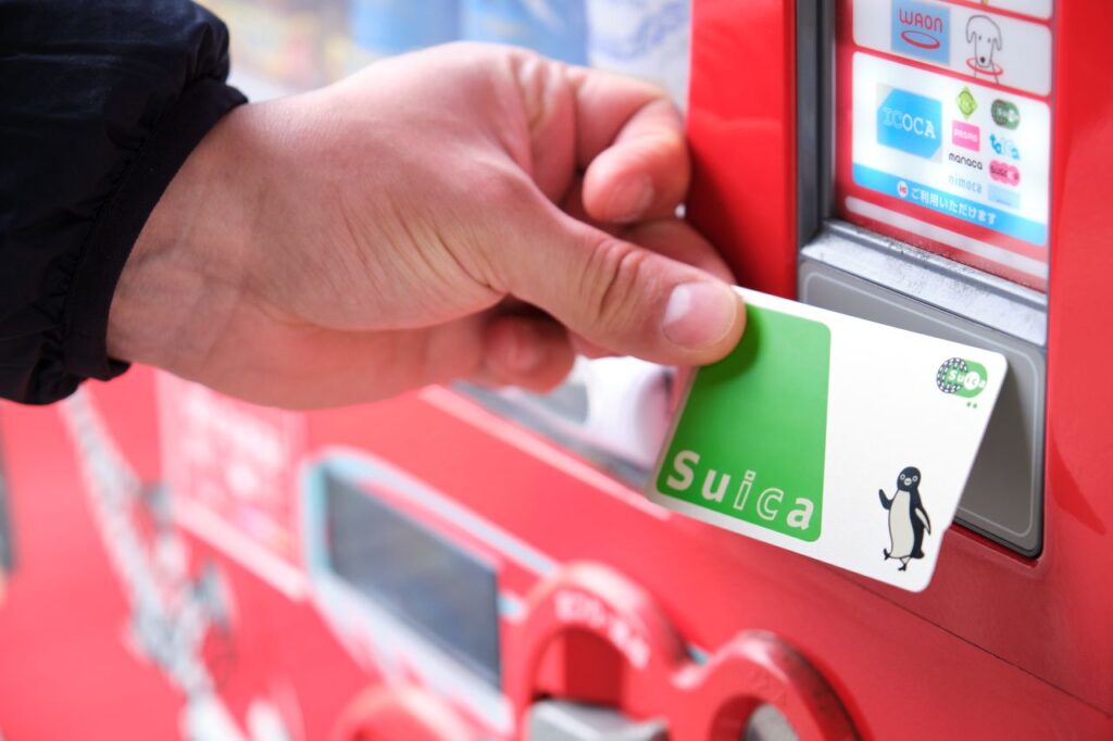 Hand tapping a Suica card on the IC card reader of a red vending machine in Japan